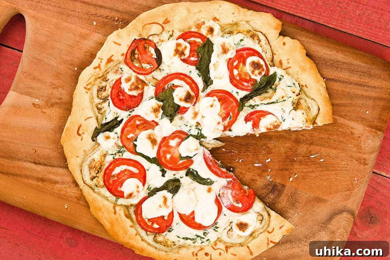 Creamy Ricotta Eggplant Pizza 2 Delicious eggplant pizza with one slice removed, topped with three cheeses, tomatoes, basil, and roasted eggplant, on a rustic cutting board