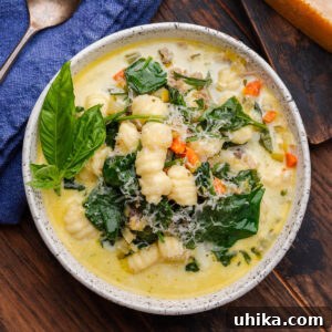 Sausage gnocchi soup in white bowl with basil garnish and grated cheese.