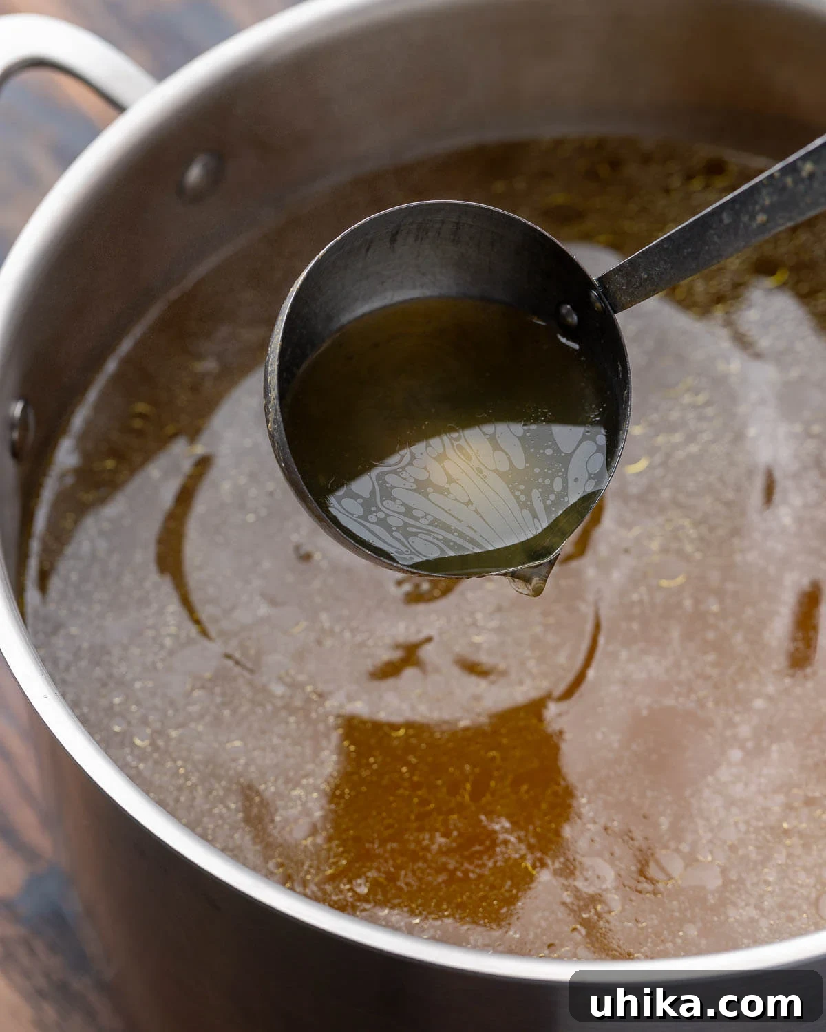 10 Must-Have Kitchen Tools for Your Fall Cooking 4 A large ladle carefully pouring rich chicken stock into a towering stainless steel stockpot, illustrating the preparation of homemade broth.