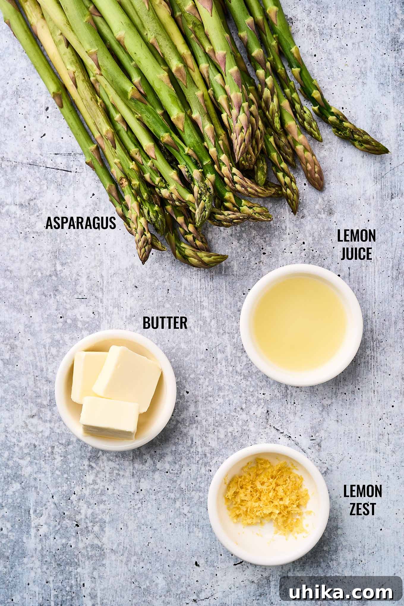 Zesty Lemon Roasted Asparagus 3 A labeled, overhead view of the ingredients needed for making lemon roasted asparagus; fresh asparagus spears, butter, lemon juice and zest.