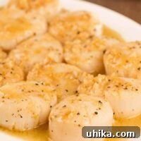 Golden Scallops with Zesty Lemon-Garlic Butter 3 Seared scallops drizzled with lemon and garlic pan sauce, served on a white plate, sprinkled with black pepper.