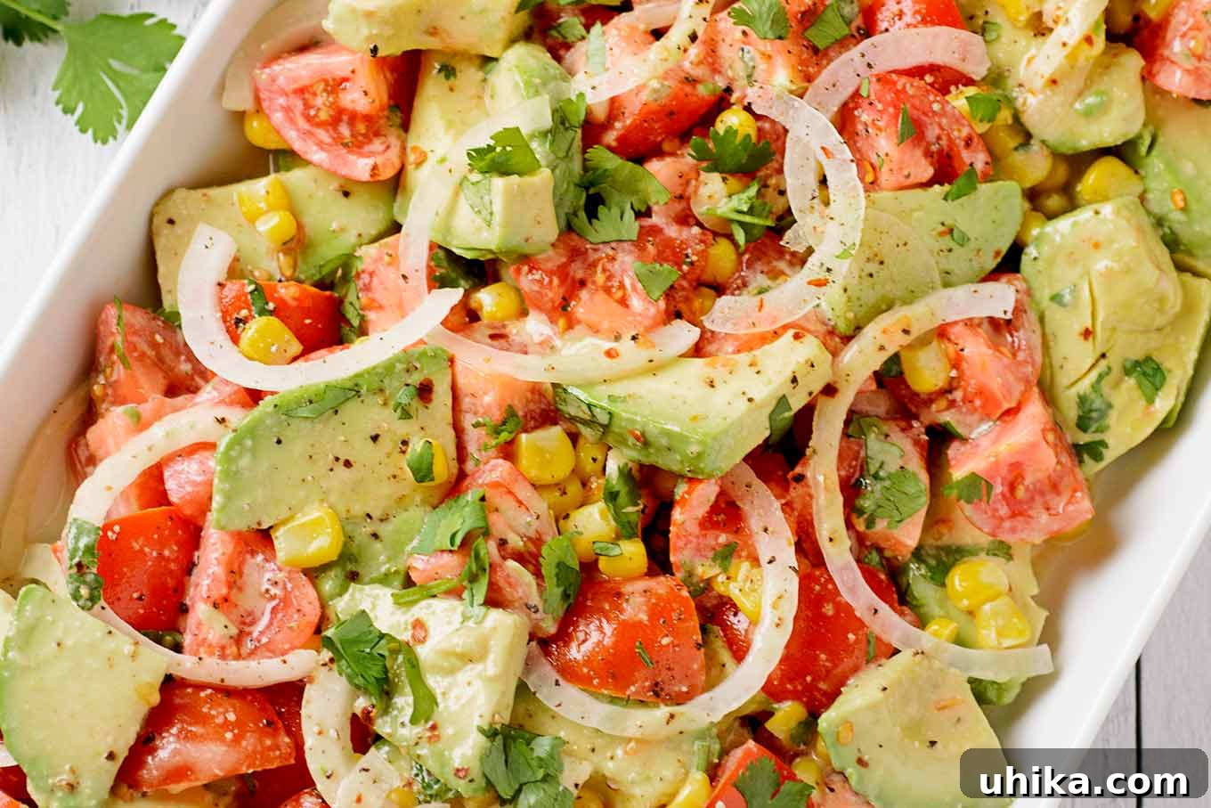 Vibrant Avocado Tomato Salad with Zesty Lime Dressing 3 A vibrant closeup of avocado tomato salad, showcasing chunks of creamy avocado, juicy tomatoes, golden corn kernels, fresh cilantro, and a sprinkle of red pepper flakes, all coated in a luscious lime dressing.