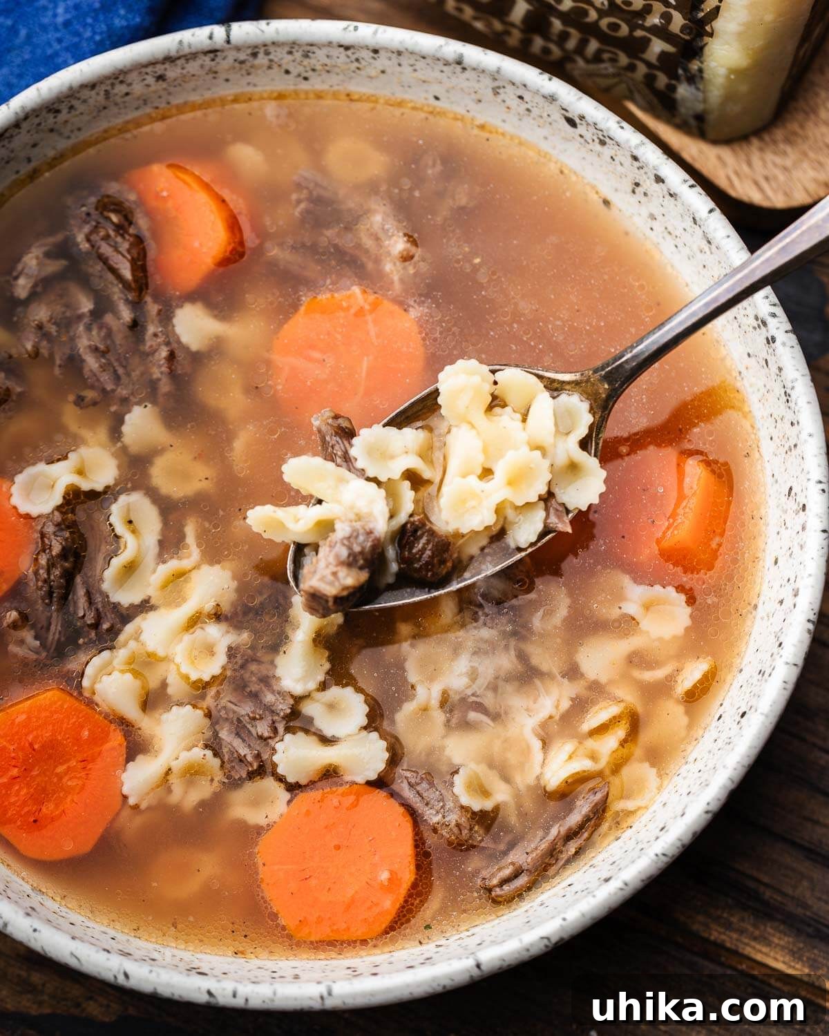Hearty Italian Beef Soup 2 Spoon holding pasta and shredded beef above bowl of soup, showcasing the rich Italian Beef Soup.