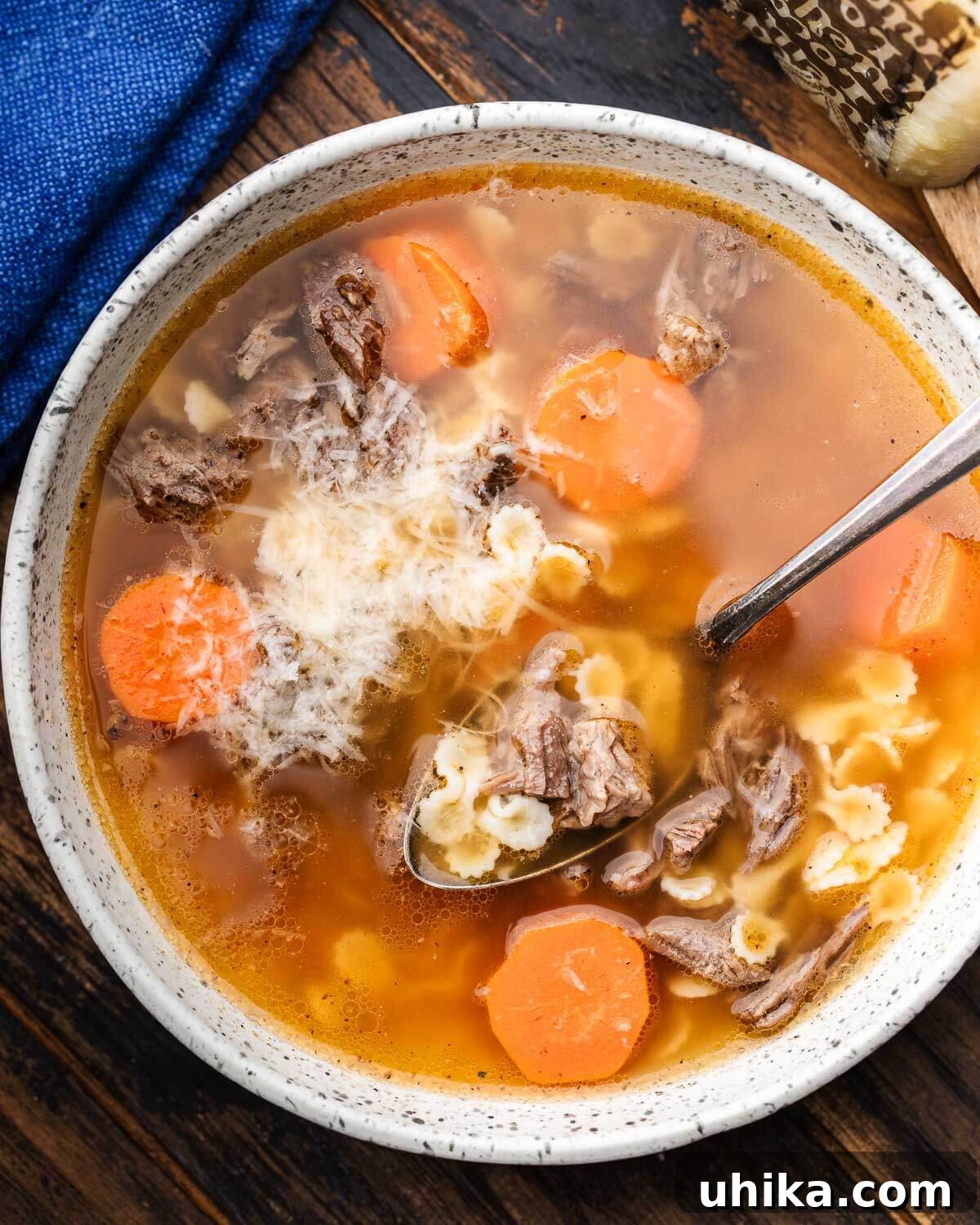 Hearty Italian Beef Soup 6 White bowl with Italian beef soup, garnished with Pecorino Romano, with a block of cheese in the background.
