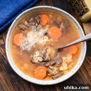 Hearty Italian Beef Soup 7 White bowl with Italian beef soup and block of Pecorino Romano in the background.