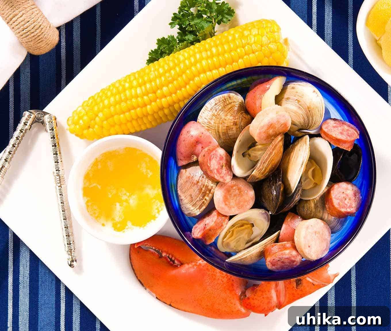 Seaside Simmer at Home 3 Plate containing lobster claw, ear of corn, bowl of melted butter, nutcracker, and bowl of steamed clams, mussels, sausage, and potatoes.