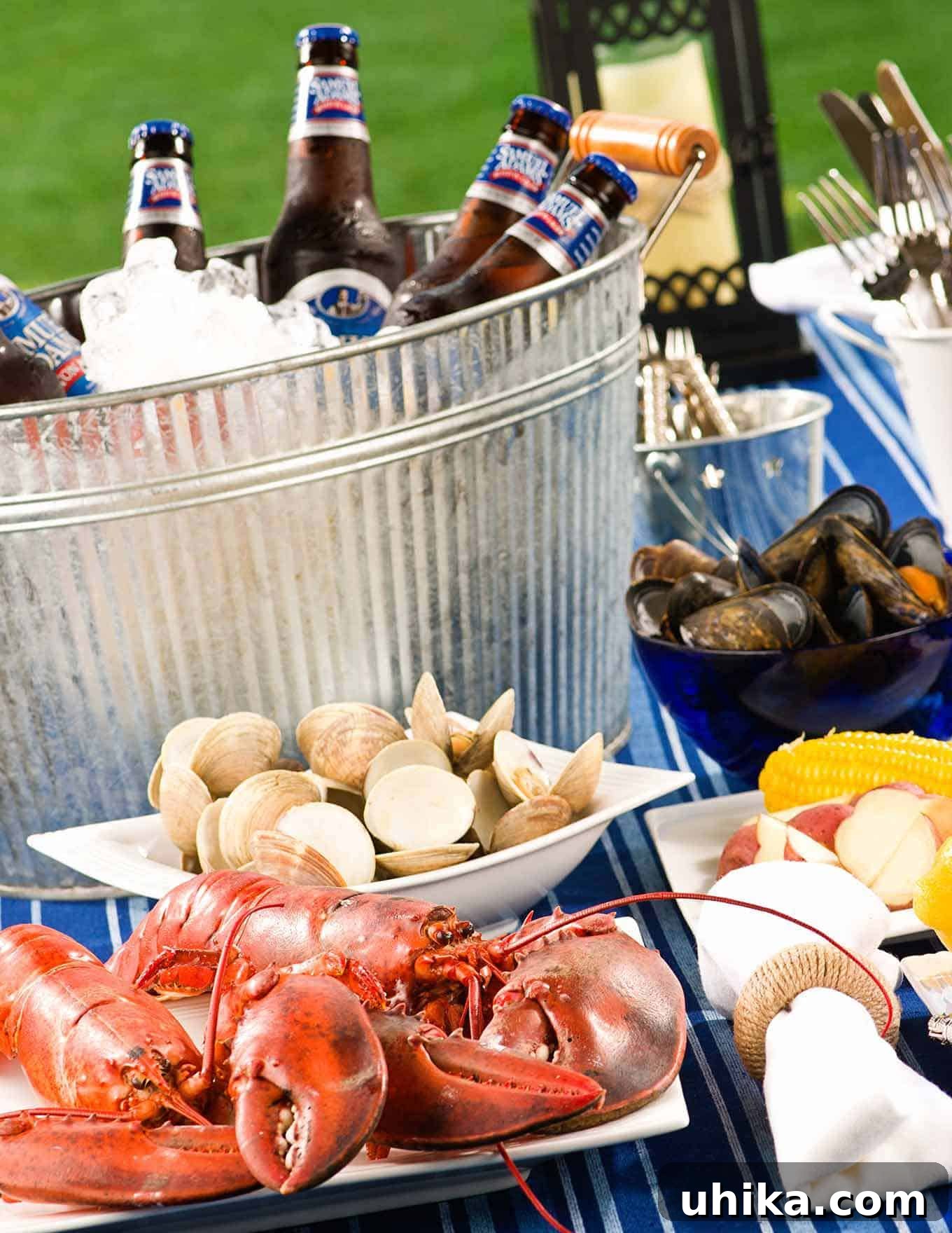 Seaside Simmer at Home 6 Table filled with with lobsters, clams, mussels, potatoes, corn, utensils, and an ice-filled bucket with cold bottles of beer.