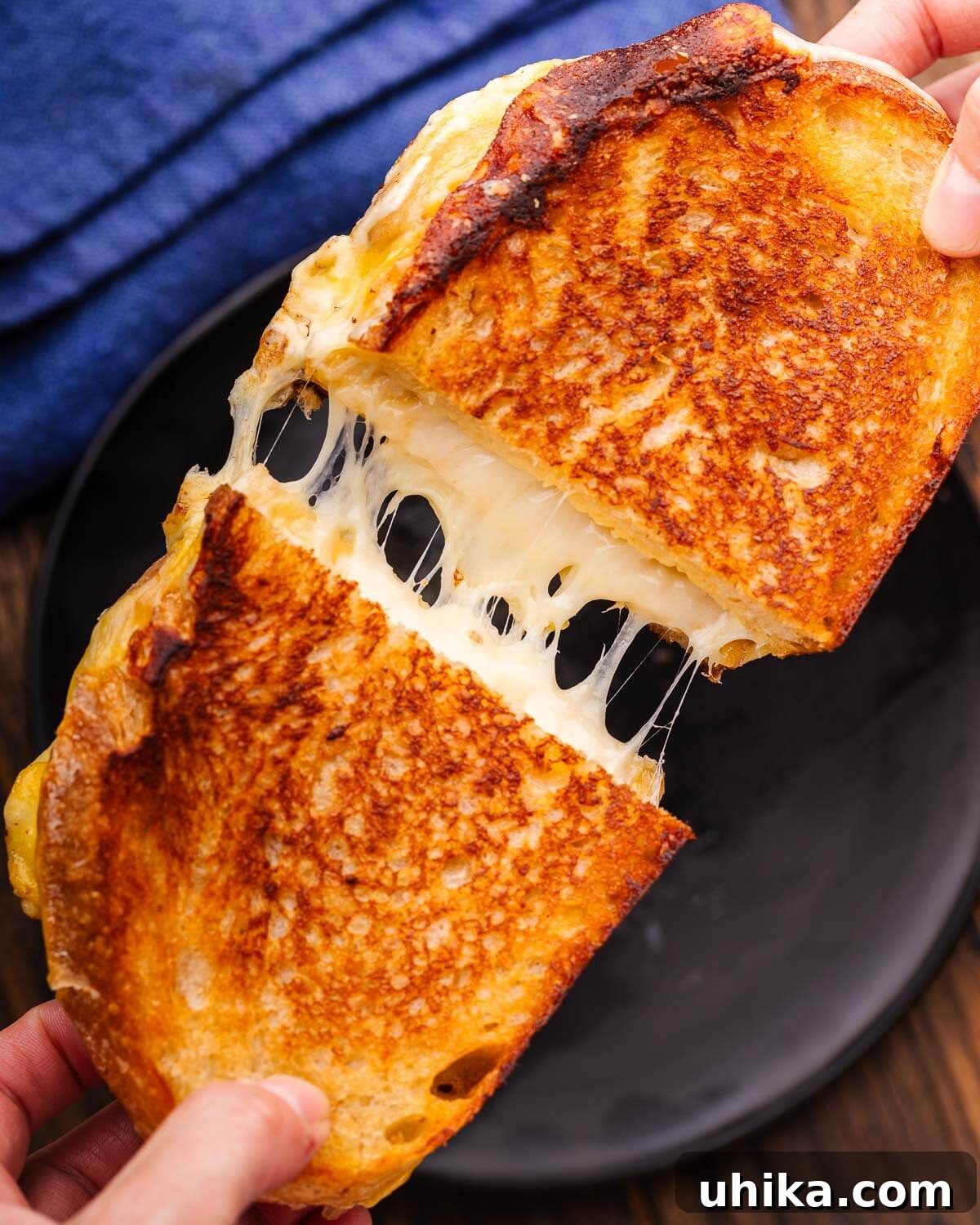 Perfectly Golden Grilled Cheese Indulgence 6 Hands pulling apart a sourdough grilled cheese sandwich over a black plate, showing the melted cheese pull.