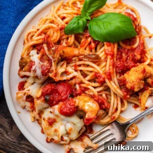 White plate with shrimp parmigiana, spaghetti, and basil garnish.
