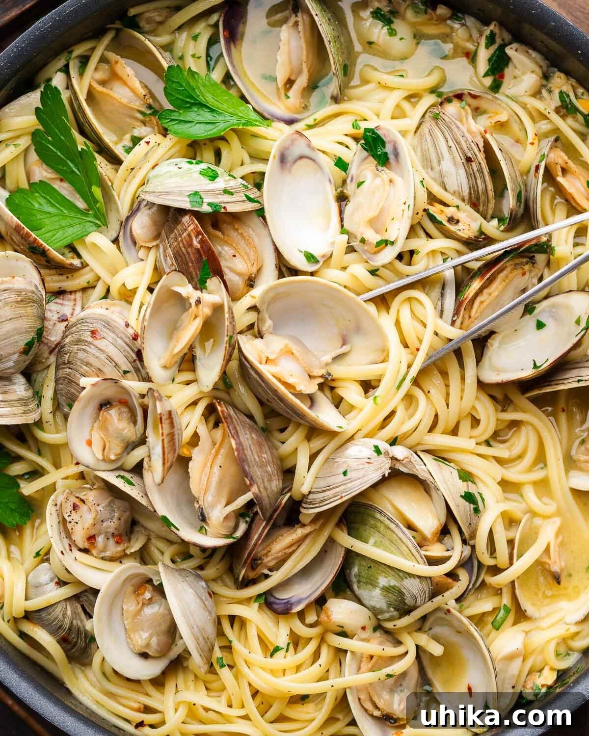 Linguine alle vongole in black pan with numerous open whole clams and parsley garnish.