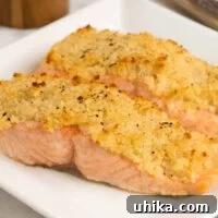 Two fillets of roasted salmon with a golden horseradish and crumb crust on a white square plate.