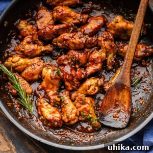 Black pan with balsamic braised chicken wings and rosemary garnish and wooden spoon.