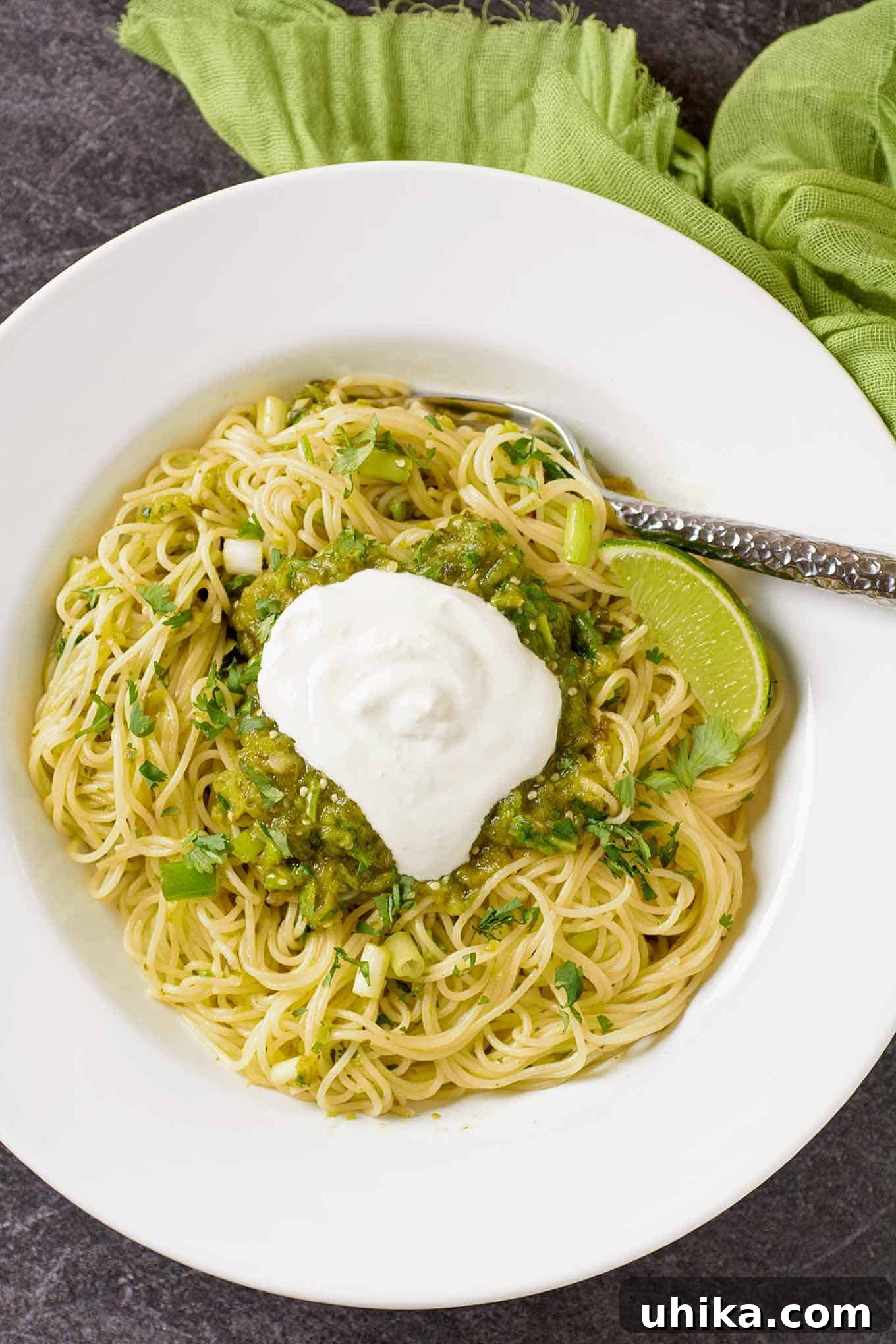 Emerald Pasta 2 Thin spaghetti tossed with a vibrant green salsa verde made with roasted tomatillos, poblano peppers, fresh lime, scallions, and cilantro, elegantly garnished with a dollop of sour cream and a lime wedge.