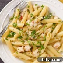 A plate of penne pasta tossed with tender lobster, shallots, white wine, cream, butter, and a drizzle of truffle oil, garnished with chopped parsley.
