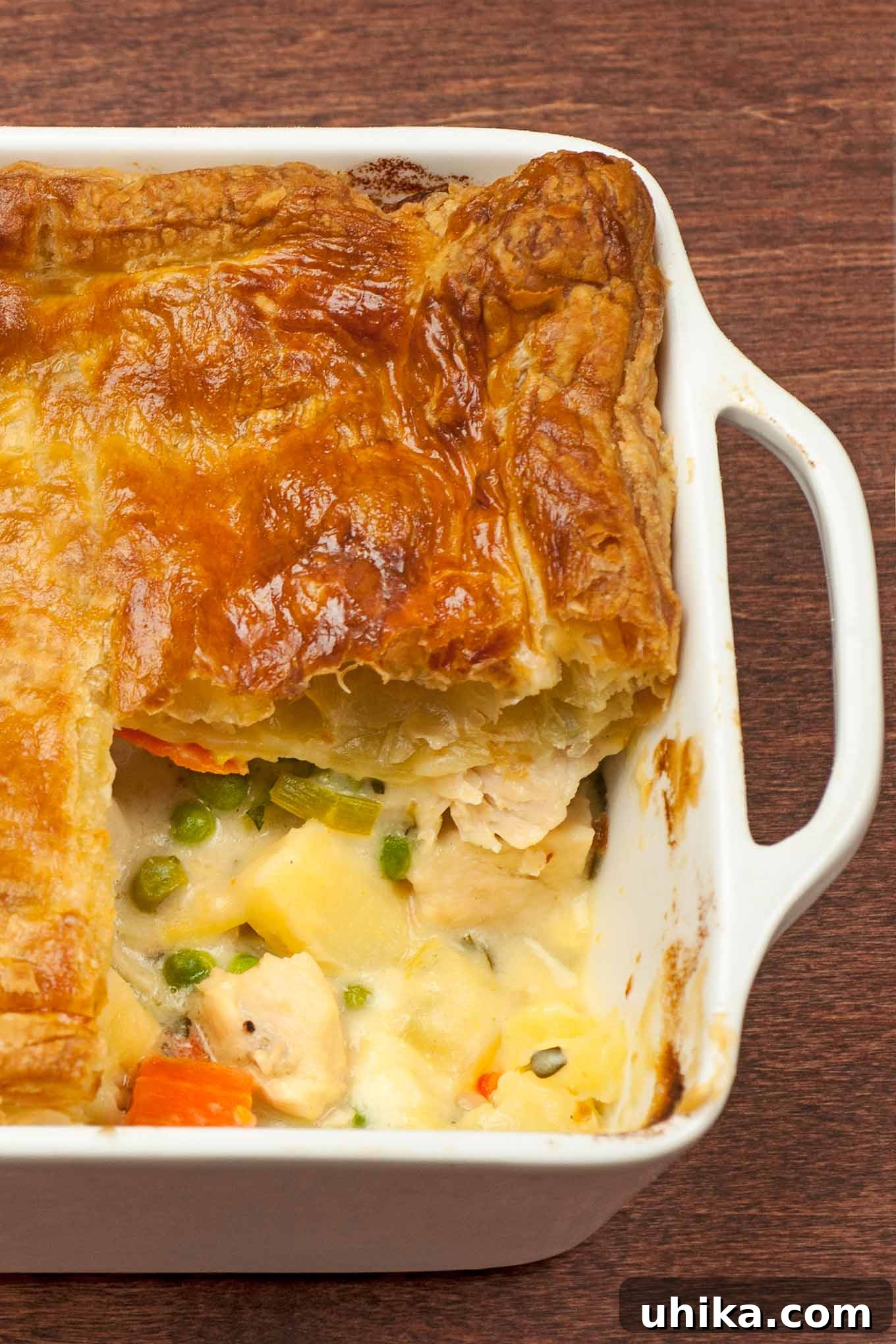 Golden Puff Pastry Chicken Pot Pie 2 Pot pie baking dish with a single serving removed showing layers of flaky pastry and creamy chicken filling.