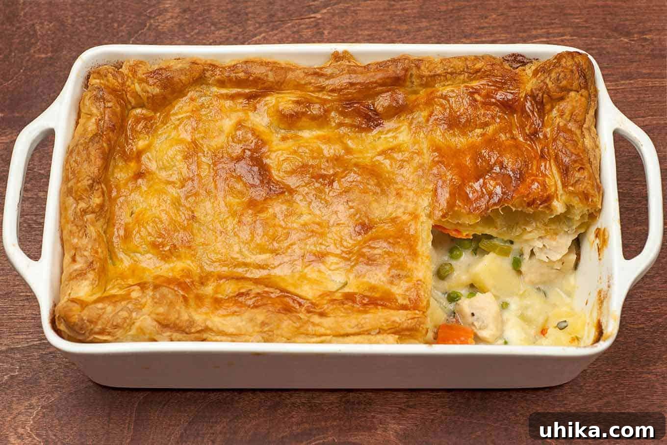Golden Puff Pastry Chicken Pot Pie 3 Pot pie baking dish with a single serving removed showing layers of flaky pastry and creamy chicken filling.