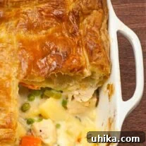 Pot pie baking dish with a single serving removed showing layers of flaky pastry and creamy chicken filling.