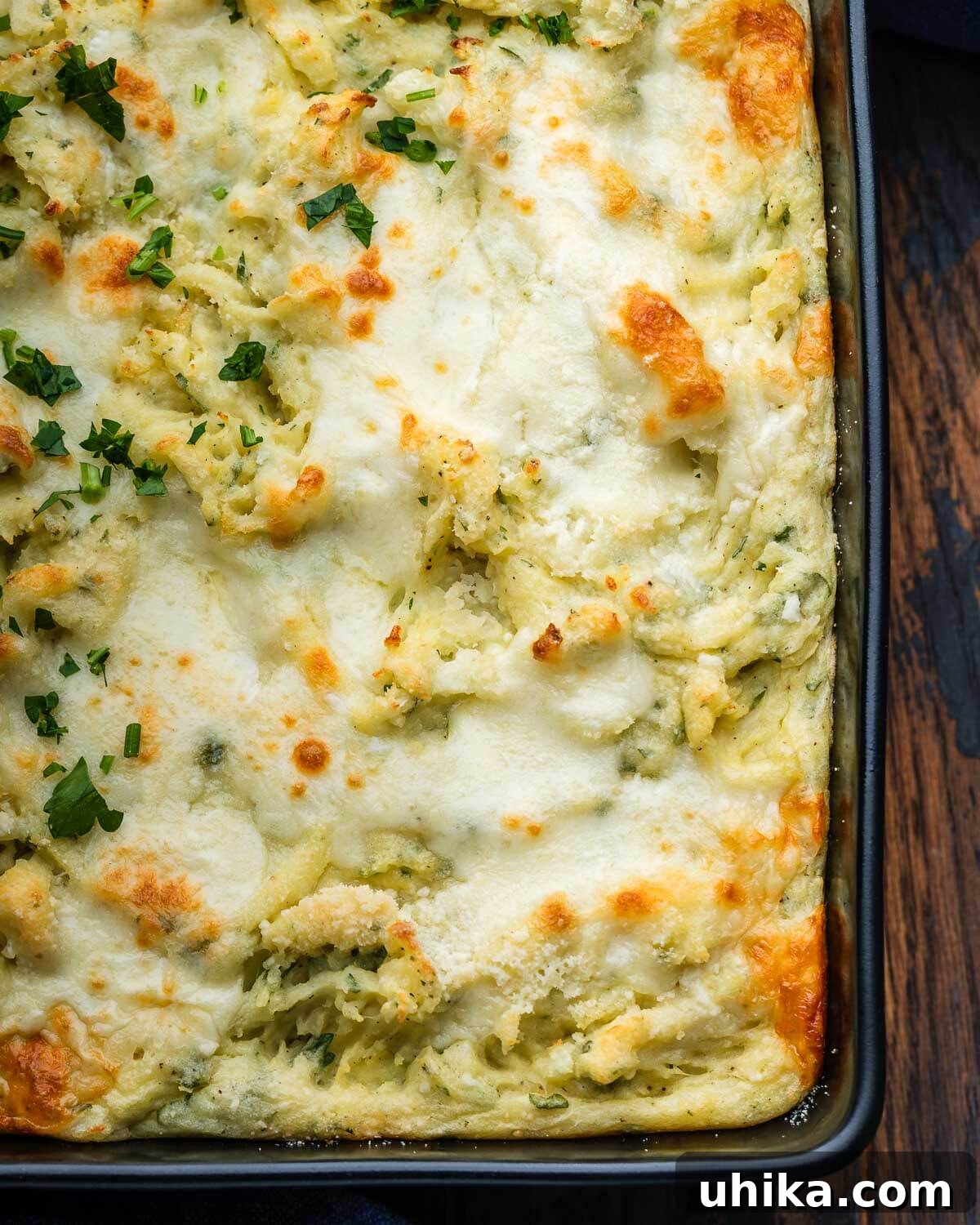 Baked Parmesan Mashed Potatoes 5 A close-up shot of the black baking dish filled with golden and bubbly Italian baked mashed potatoes, showing the cheesy topping and creamy texture.