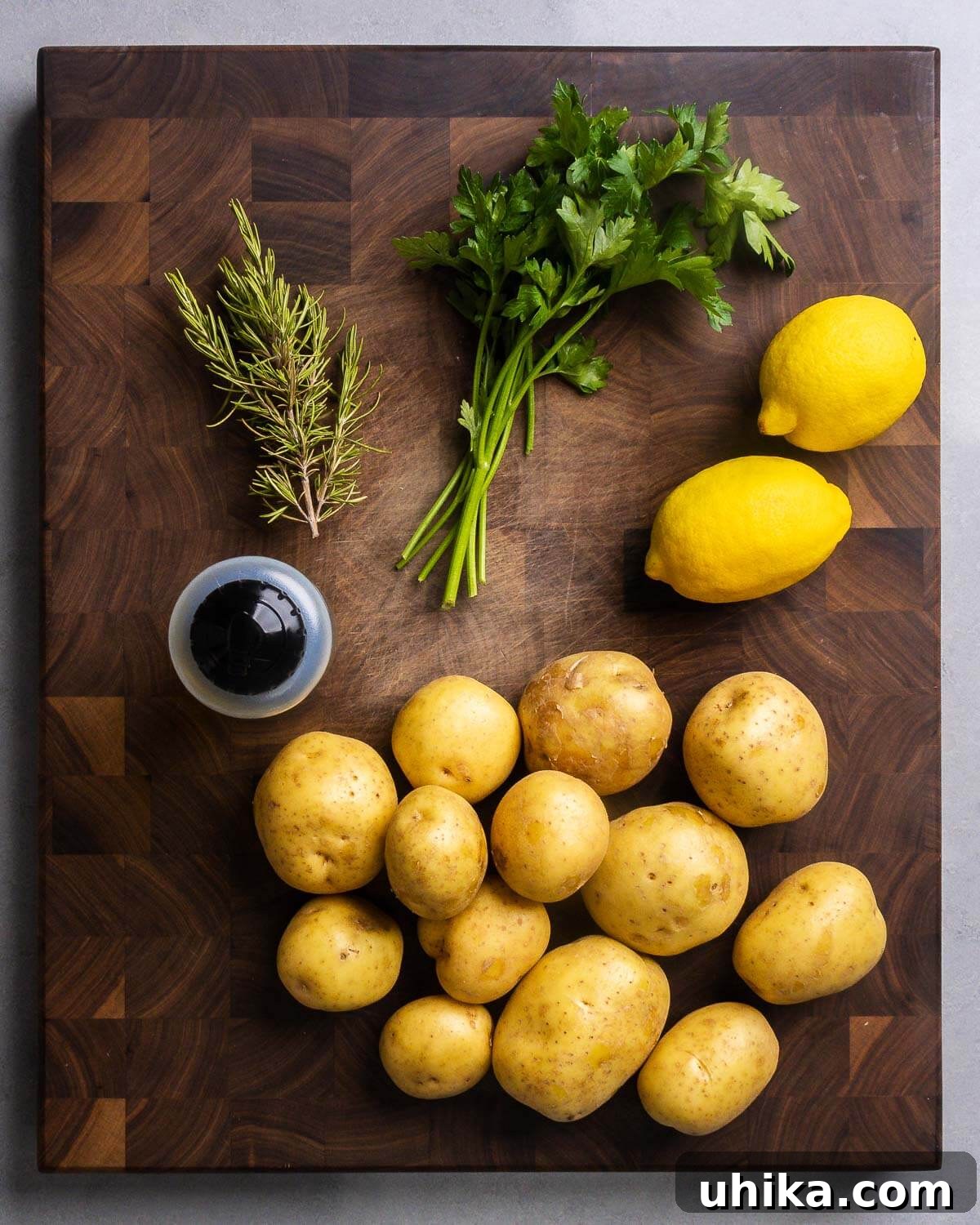 Crispy Rosemary Lemon Smashed Potatoes 3 Fresh ingredients laid out on a surface: bundles of vibrant green rosemary and parsley, bright yellow whole lemons, a glass bottle of extra virgin olive oil, and a pile of golden Yukon Gold potatoes.