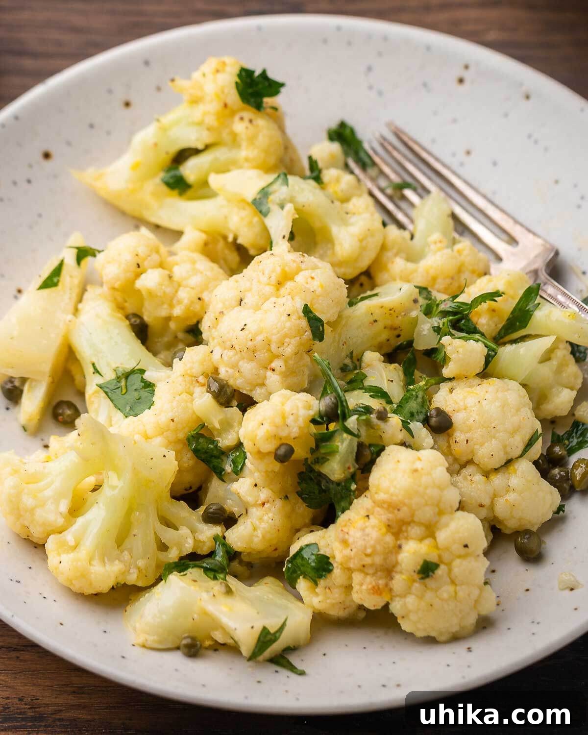 Closeup shot of Italian cauliflower salad garnished with fresh herbs in a white plate, highlighting its vibrant colors and appealing texture.