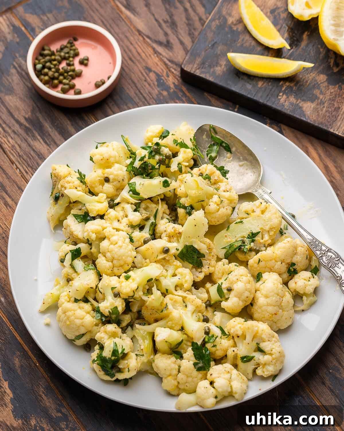 Beautifully arranged Italian cauliflower salad in a white platter, garnished with fresh parsley, alongside whole lemons and a scattering of capers, ready to be served.