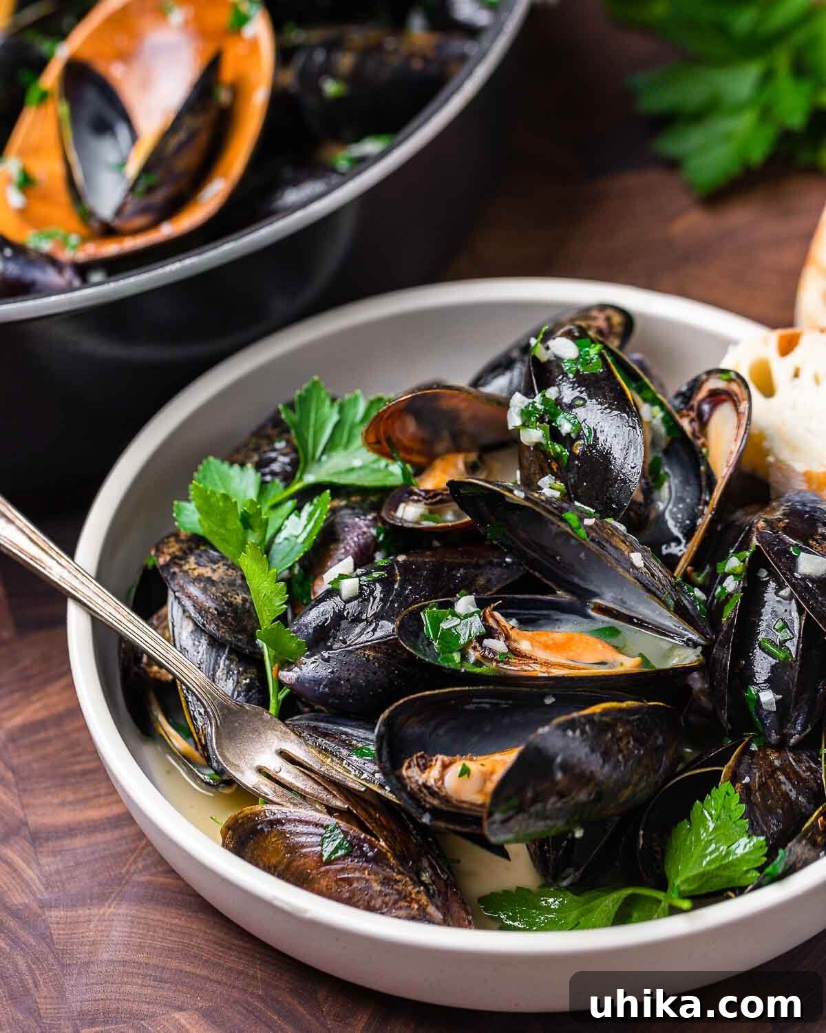 Seafood Spectacle: Recipes for Your Seven Fish Feast 11 White bowl filled with perfectly steamed mussels in a rich white wine sauce, served with a tiny fork.