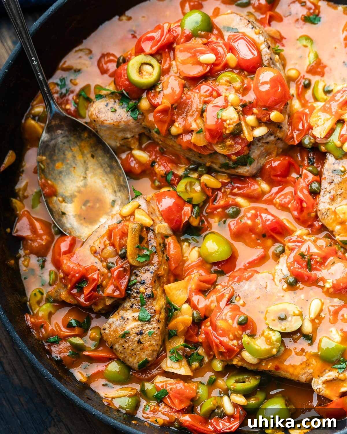 Tuna Siciliana: Olives and Capers 7 Black pan with Sicilian-style tuna smothered in olive, garlic, tomato, and pine nut sauce, ready to be served.
