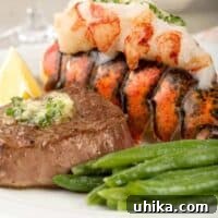 A closeup view of a pan-seared filet mignon topped with parsley butter next to a lobster tail with its juicy meat on top, and a serving of green beans. This is an easy recipe for a restaurant-quality surf and turf dinner at home.