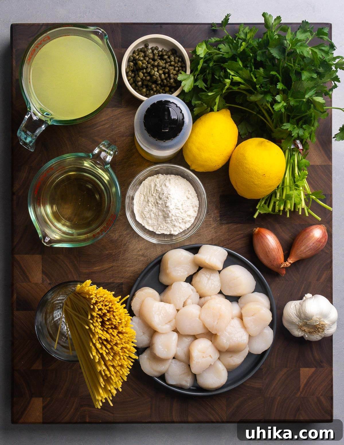 Pan Seared Scallops with Lemon Garlic Pasta 3 Ingredients shown: chicken stock, capers, olive oil, lemons, parsley, wine, flour, shallots, linguine, scallops, and garlic.