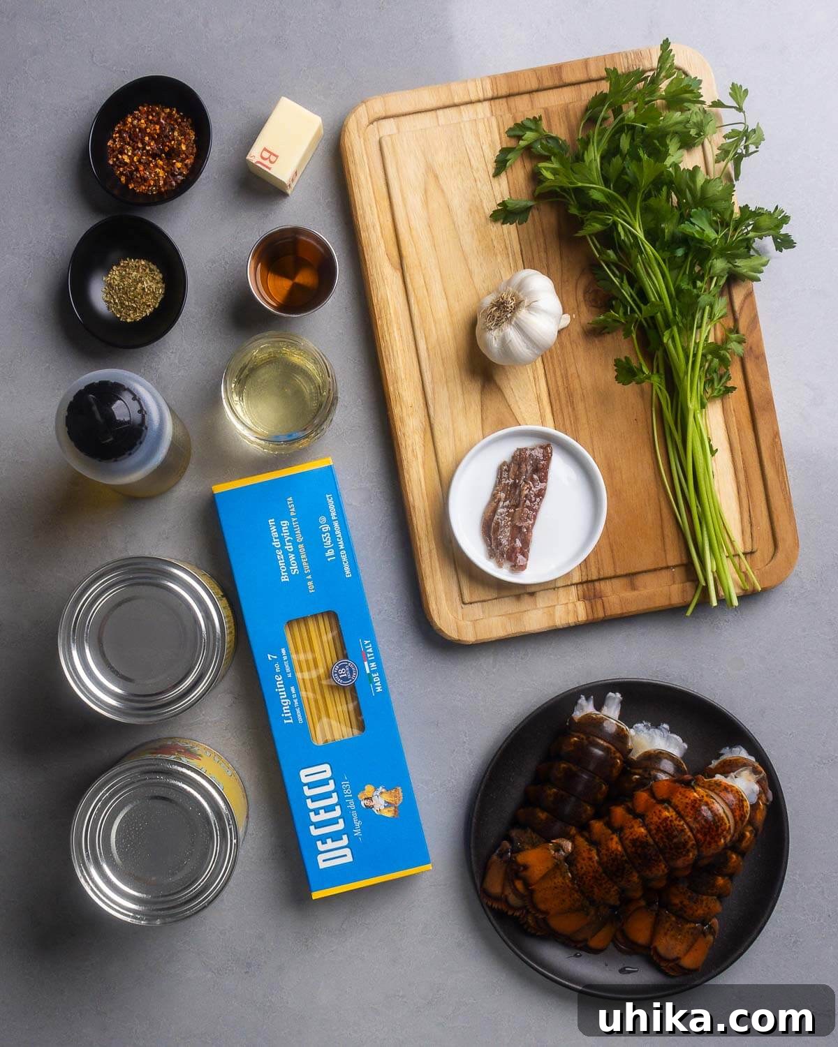 Inferno Lobster 3 A flat lay of ingredients for Lobster Fra Diavolo: hot red pepper flakes, dried oregano, butter, brandy, dry white wine, olive oil, fresh garlic, parsley, anchovy fillets, canned plum tomatoes, linguine pasta, and raw lobster tails.