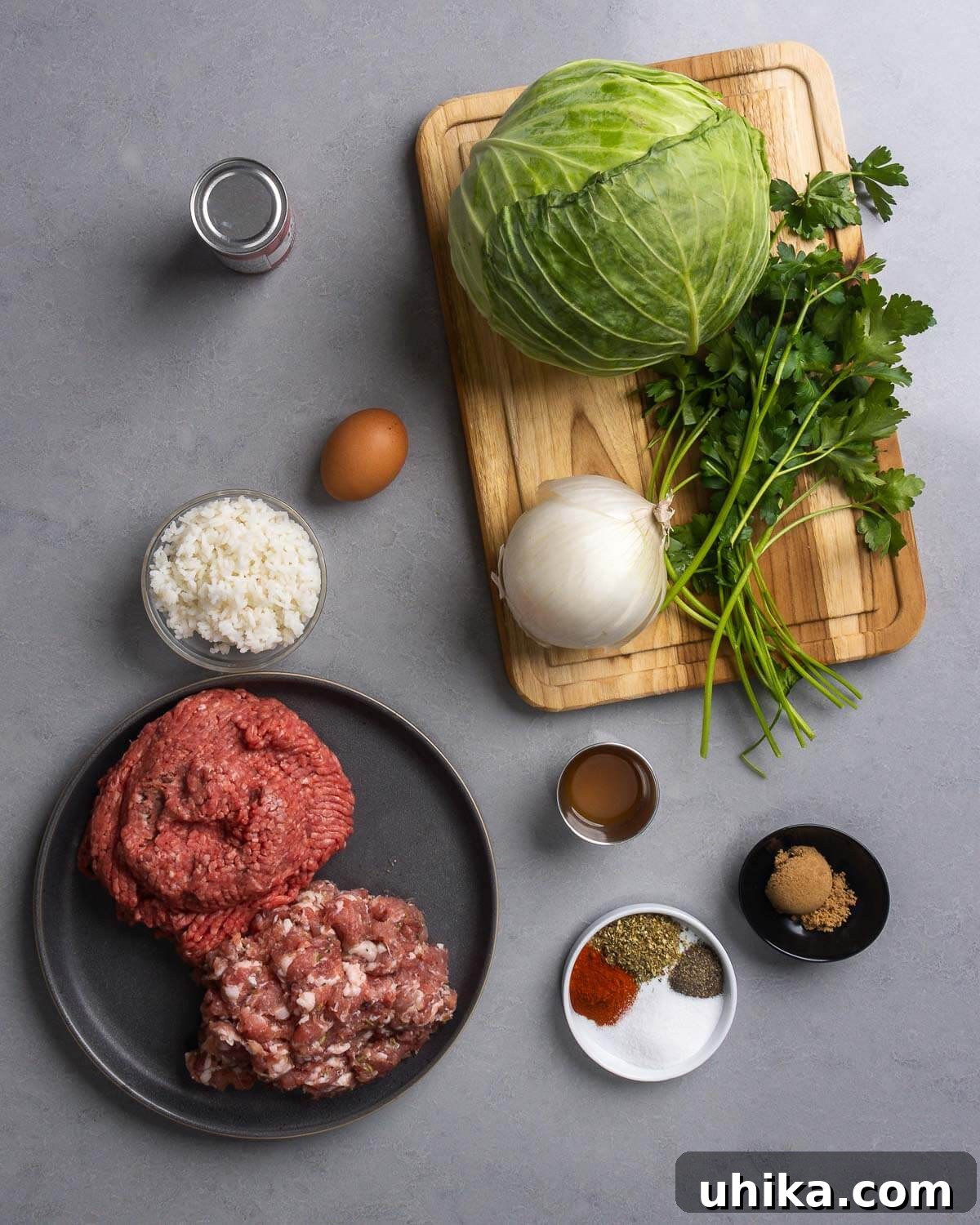 Savory Cabbage Wraps 3 Ingredients for stuffed cabbage rolls laid out: tomato paste, egg, rice, cabbage, parsley, onion, ground chuck, bulk sausage, cider vinegar, various spices, and brown sugar.