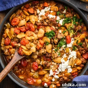 Black pan with Greek beans and sausage (Fassolada me Loukaniko) with spoon and blue napkins.