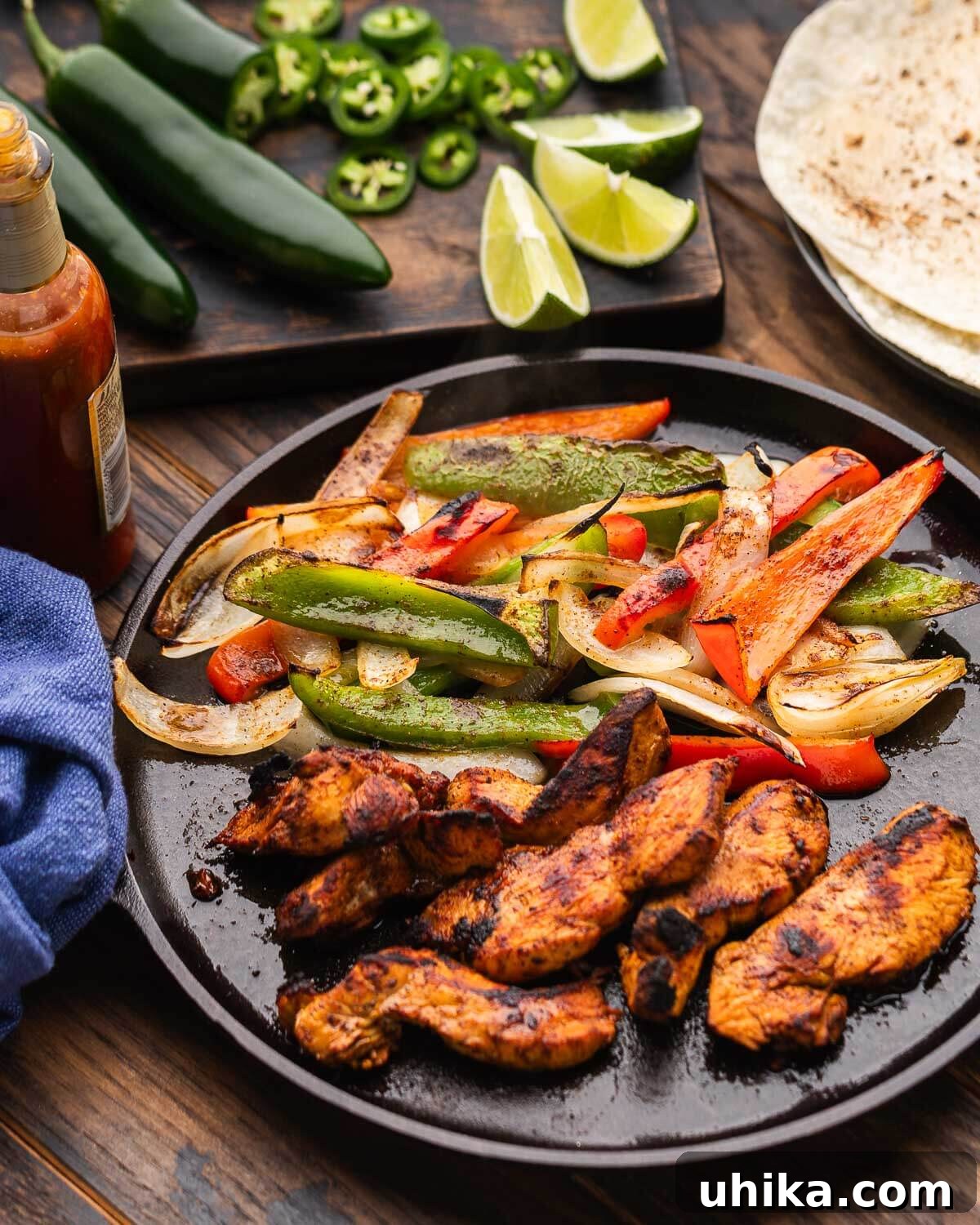 Sizzling Chicken Fajita Fiesta 6 Small cast iron pan with chicken fajitas and jalapenos, limes, and tortillas in the background.