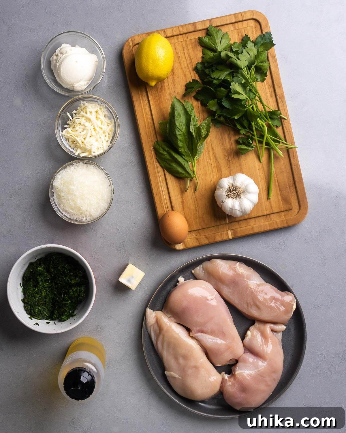 Effortless Spinach Stuffed Chicken 3 Ingredients for Spinach Stuffed Chicken Breasts: ricotta, mozzarella, parmesan, lemon, basil, parsley, garlic, spinach, olive oil, butter, and chicken breasts laid out on a wooden board.