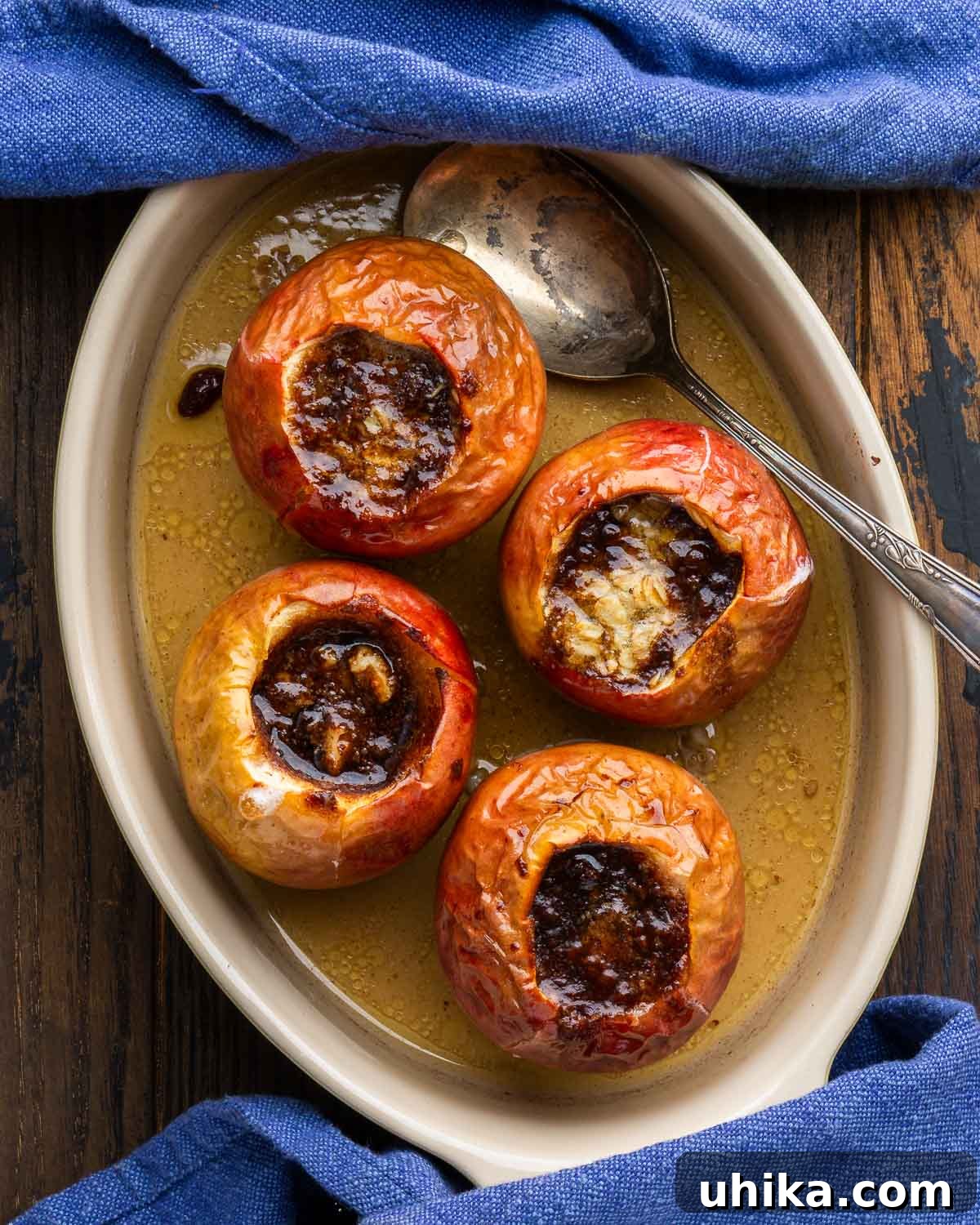 Simple Homestyle Baked Apples 2 Four baked apples nestled in a glass baking dish, adorned with blue napkins, ready to be served.