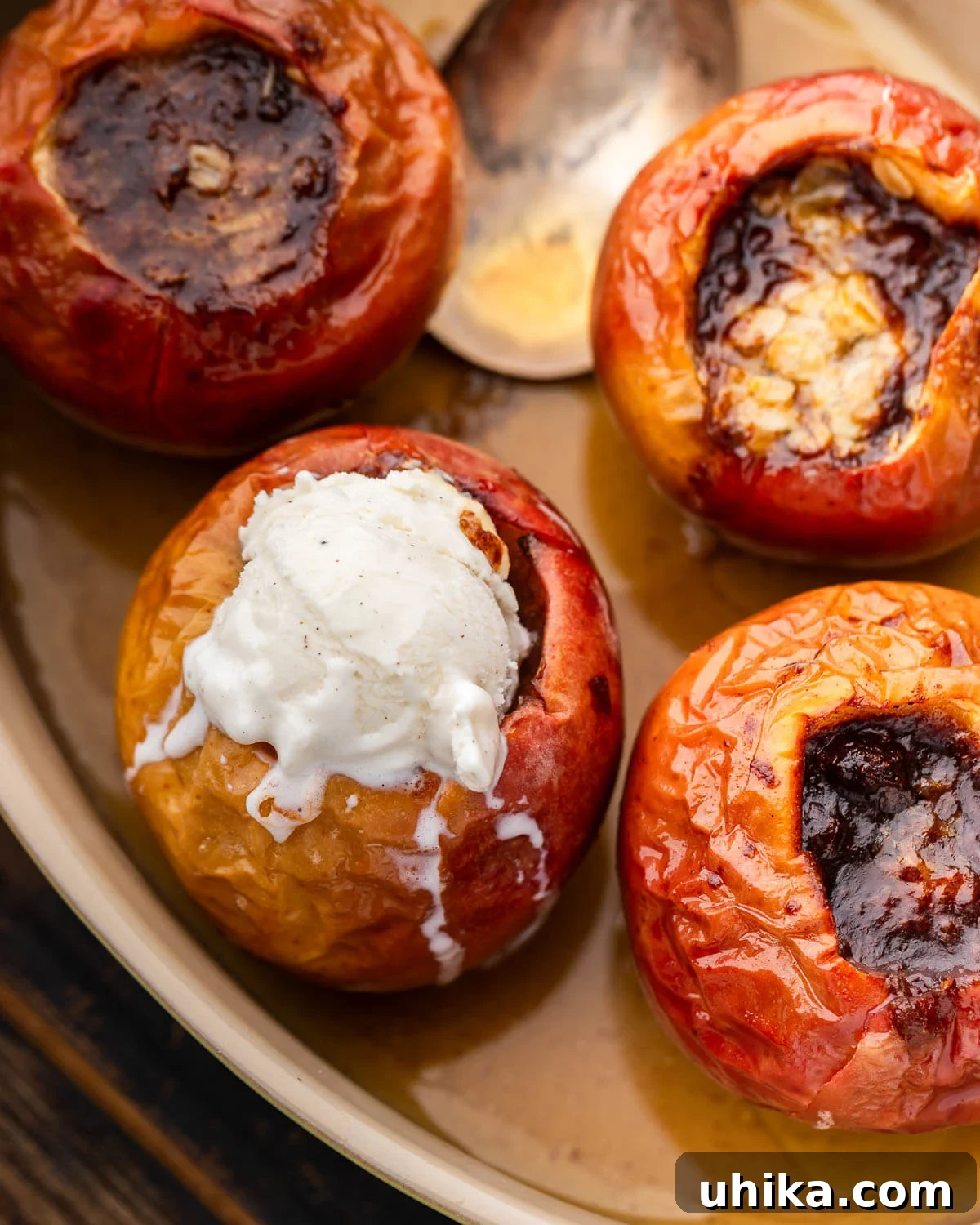 Simple Homestyle Baked Apples 5 Two baked apples in a baking dish, one with a scoop of vanilla ice cream melting inside its core.