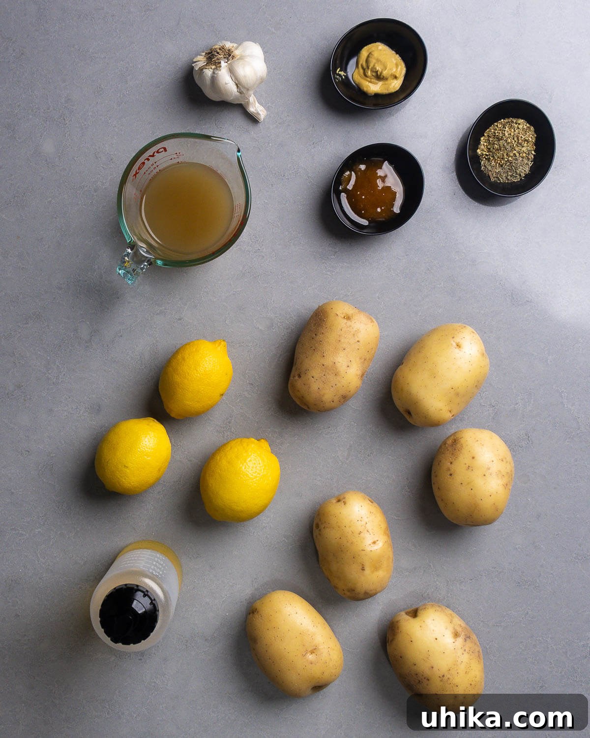 Zesty Lemon Oregano Roasted Greek Potatoes 3 Ingredients shown for Greek lemon potatoes: fresh garlic, chicken stock, a touch of honey, Dijon mustard, Greek oregano, several lemons, peeled Yukon Gold potatoes, and olive oil.