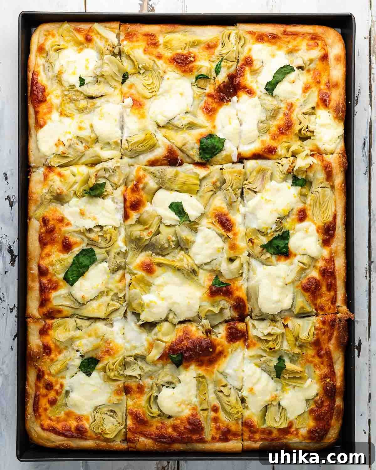 Mediterranean Artichoke Pizza 2 Overhead shot of artichoke sheet pan pizza on white board, showcasing its rich toppings and golden crust.