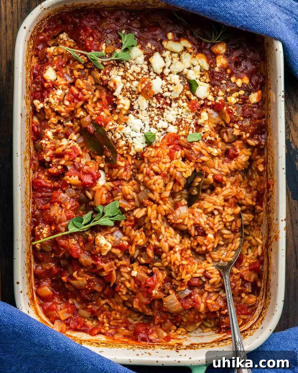 Mediterranean Orzo Bake 2 Golden baked orzo topped with melted feta cheese in a rustic baking dish, garnished with fresh herbs.