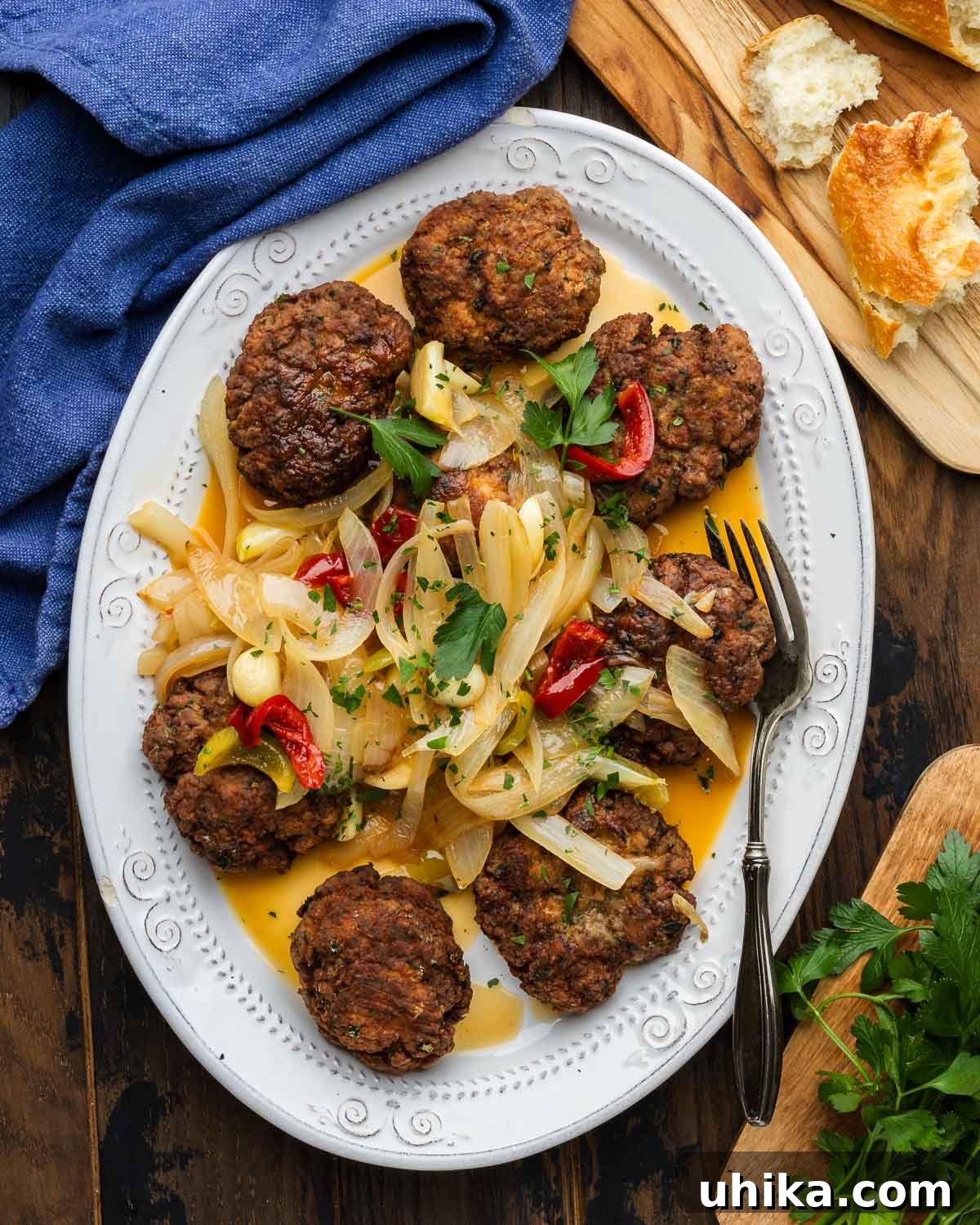 Perfect Pan Fried Meatballs 2 Pan fried meatballs topped with onions and cherry peppers in white platter along with loaf of bread on the side.