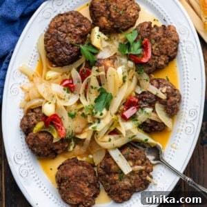 Pan fried meatballs topped with onions and cherry peppers in white platter.