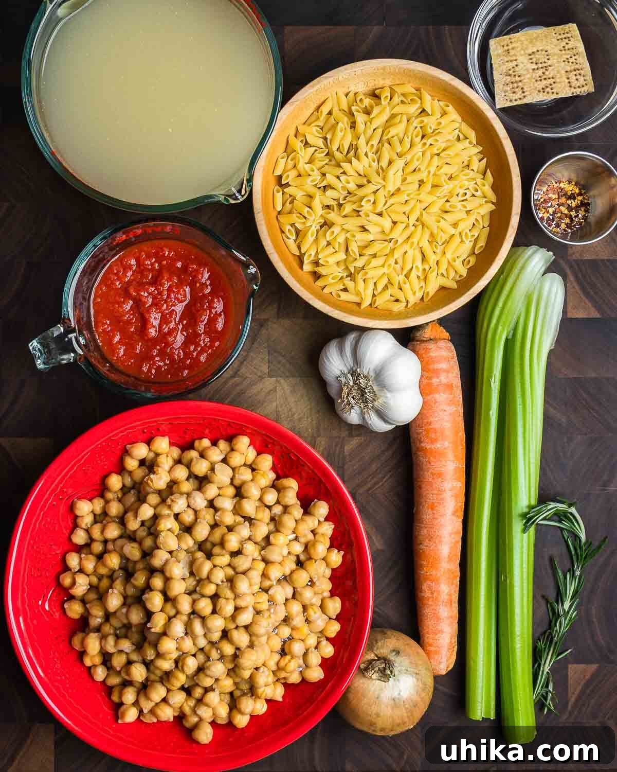 Hearty Pasta and Chickpeas 4 Ingredients shown: vegetable stock, small pasta, parmesan rind, hot red pepper flakes, crushed tomatoes, garlic, carrot, celery, chickpeas, onion, and rosemary.