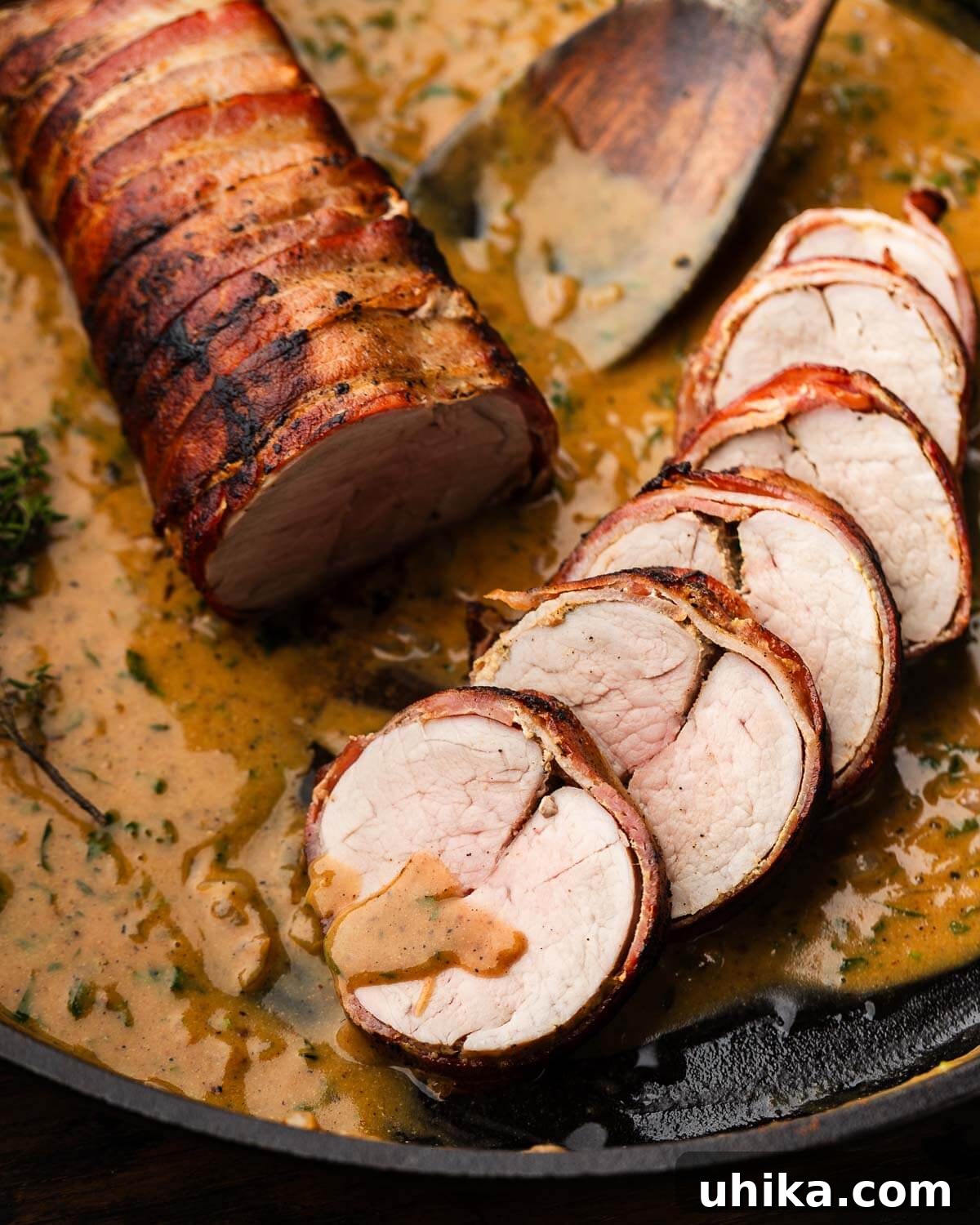 Perfectly sliced bacon-wrapped pork tenderloin with a luscious creamy mustard sauce resting in a pan, ready to serve.