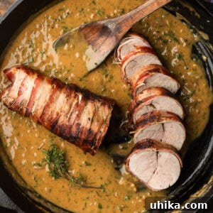 Sliced bacon wrapped pork tenderloin with creamy mustard sauce in cast iron pan.
