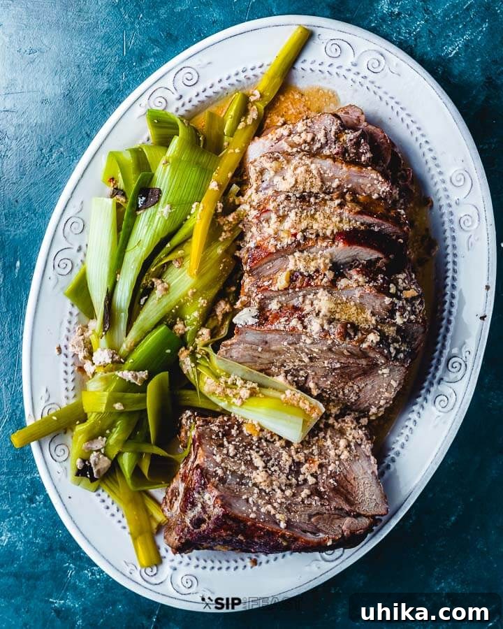Maiale Al Latte - sipandfeast.com #maialeallatte #dinner #italianrecipe Slices of tender milk-braised pork (Maiale al latte) arranged on a platter with soft, golden leeks, all generously coated in the rich, nutty milk sauce.