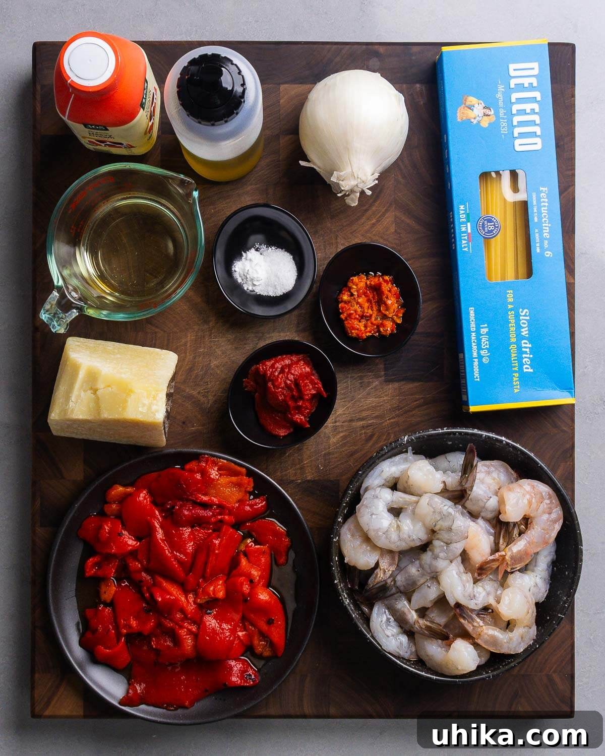 Velvety Roasted Red Pepper Shrimp Pasta 4 An assortment of fresh ingredients laid out for creamy roasted red pepper pasta with shrimp, including heavy cream, olive oil, a whole onion, dry pasta, white wine, baking soda, Calabrian chili paste, tomato paste, Pecorino Romano cheese, a jar of roasted red peppers, and raw shrimp.