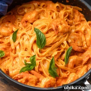 Roasted red pepper pasta with shrimp in black pan garnished with basil leaves.
