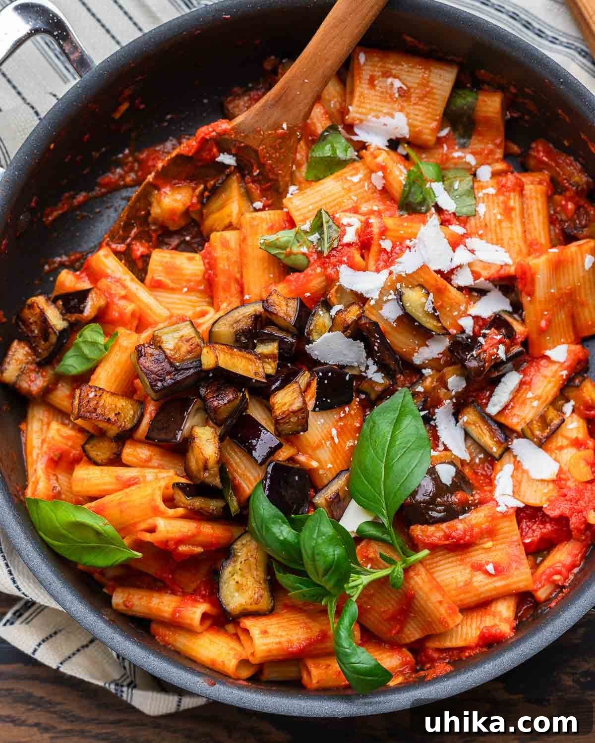 Sicilian Masterpiece Eggplant Pasta 8 An overhead shot of a pan filled with freshly made Pasta alla Norma, adorned with shredded ricotta salata and vibrant basil leaves, ready to be served.