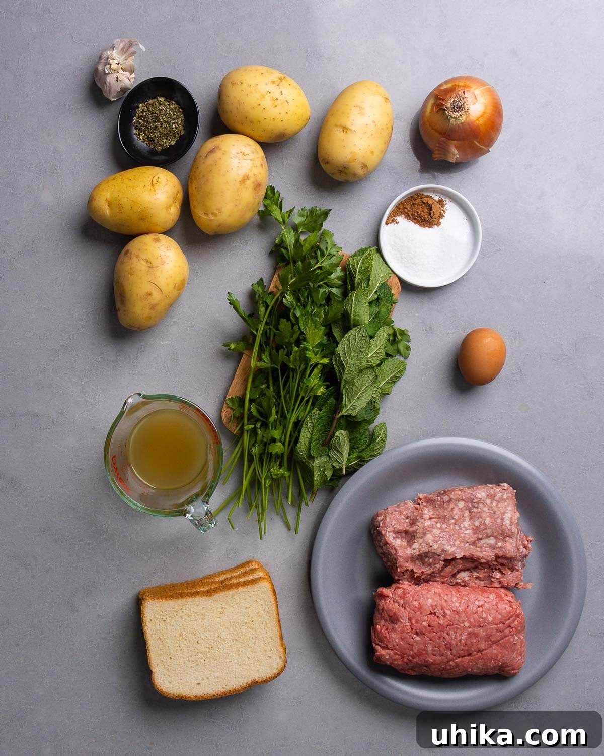 Mediterranean Sheet Pan Meatballs with Roasted Potatoes 4 A selection of fresh ingredients including garlic, oregano, potatoes, onion, nutmeg, salt, parsley, mint, egg, chicken stock, white bread, ground chuck, and ground lamb, neatly arranged for the Greek Meatballs and Potatoes recipe.