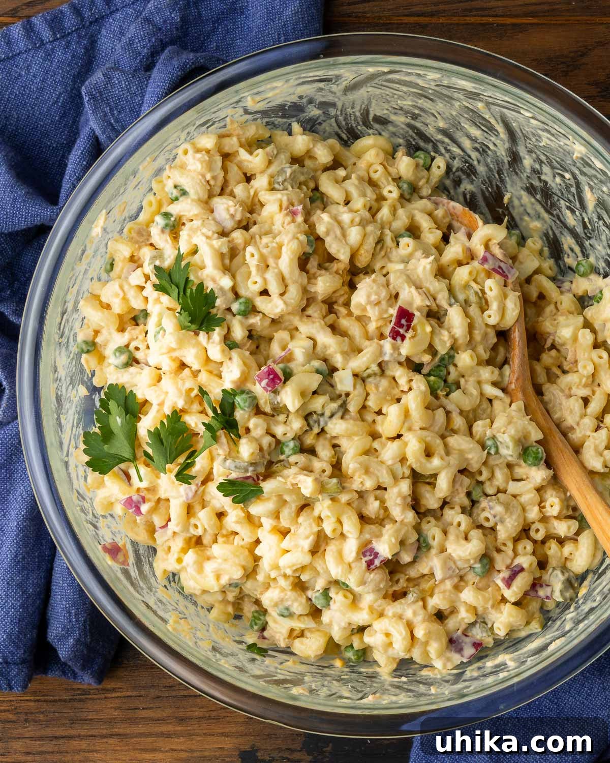Creamy Tuna Macaroni Sensation 2 Delicious Tuna Macaroni Salad served in a clear glass bowl, with vibrant blue napkins arranged beside it.